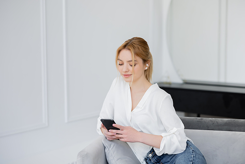 Young woman using smartphone and earphone on couch at home