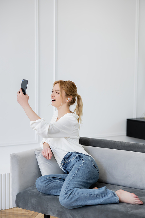 Positive woman in earphone having video call on laptop on couch at home