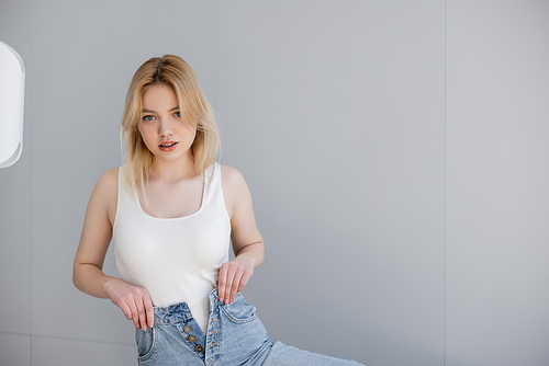 Young blonde woman in bodysuit and jeans looking at camera