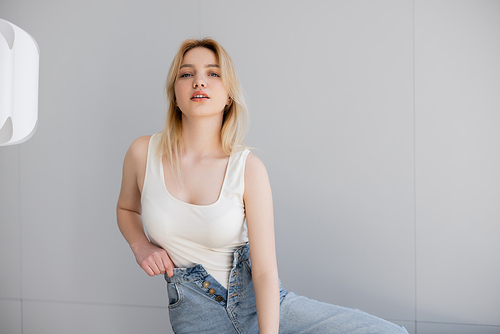 Blonde woman in jeans looking at camera at home
