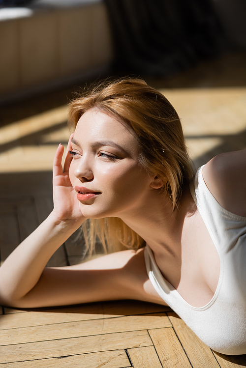 Portrait of young blonde woman looking away while lying on wooden floor