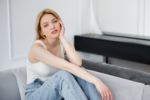 Pretty blonde woman in jeans siting on sofa at home
