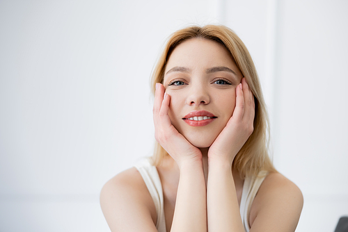 Pretty young woman touching face and looking at camera at home