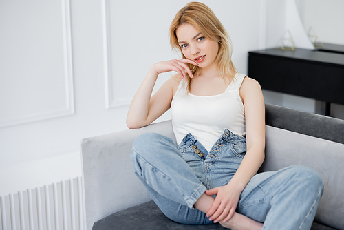 Smiling barefoot woman in jeans looking at camera on couch