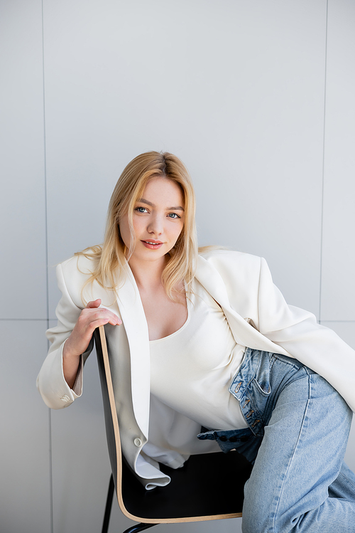 Pretty young woman in jeans and jacket smiling while sitting on chair