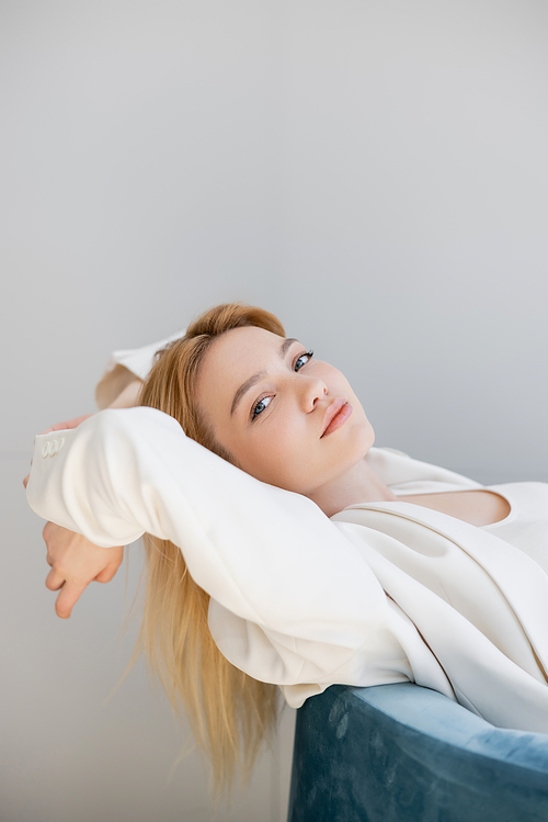 Pretty woman in jacket sitting on armchair isolated on grey