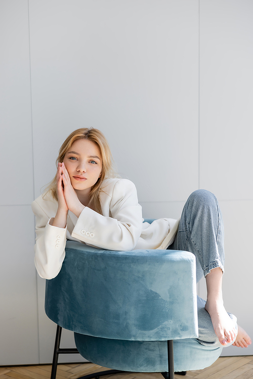 Stylish and barefoot woman sitting on blue armchair at home
