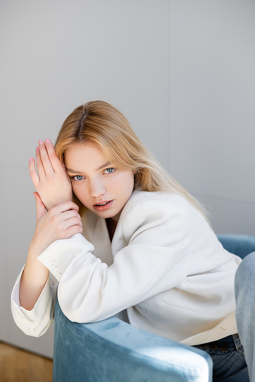 Young trendy woman sitting on velvet armchair at home