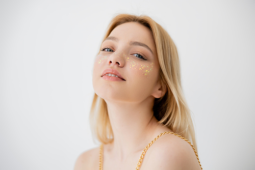 Young woman with glitter on cheeks looking at camera isolated on grey