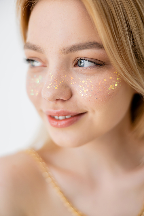 Portrait of young woman with glitter visage looking away isolated on grey
