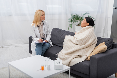 Doctor with clipboard looking at sick asian patient at home