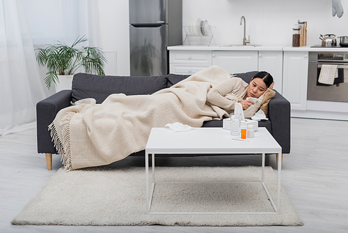 Sick asian woman suffering from runny nose and holding napkin near pills at home