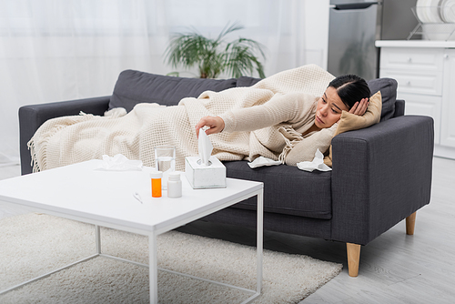 Sick asian woman taking napkin near pills and thermometer at home