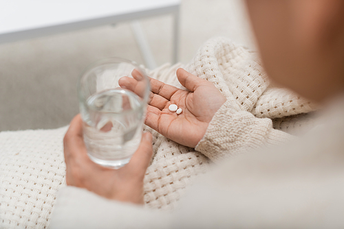 Cropped view of woman holding glass of water and pills at home