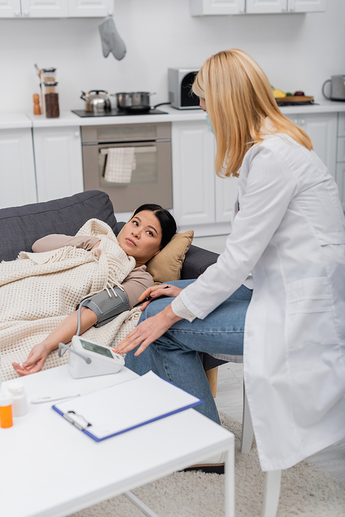 Asian patient with tonometer looking at doctor in medical mask at home