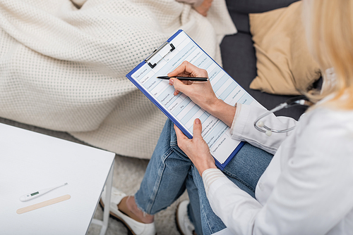 Cropped view of doctor writing on clipboard near electronic thermometer at home