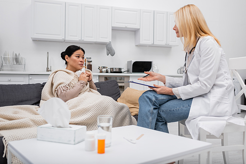 Mature doctor with clipboard pointing at sick asian patient at home