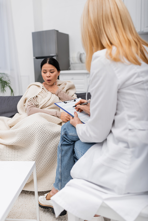 Doctor writing on clipboard near ill asian patient coughing at home