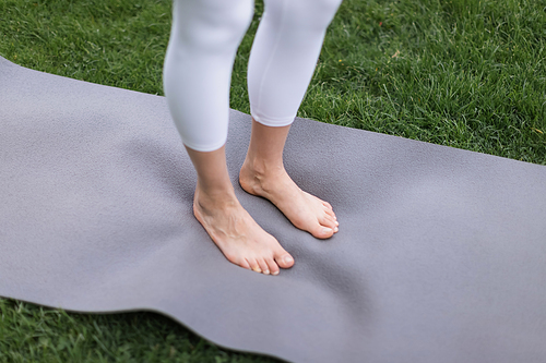 cropped view of barefoot woman in white leggings standing on yoga mat outdoors