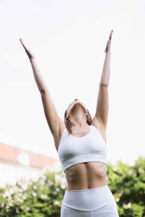 low angle view of woman in white sports bra training with raised hands outdoors