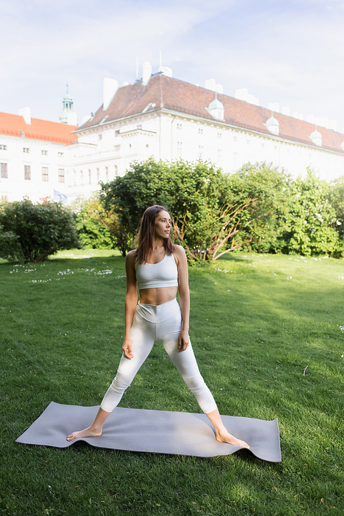 sportive woman in white sports bra and leggings standing in tree pose on yoga mat