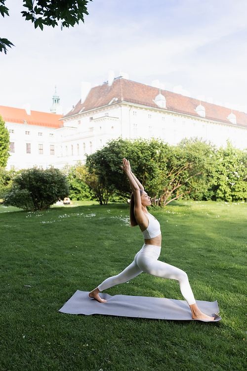 side view of sportive woman practicing crescent lunge pose on yoga mat in city park