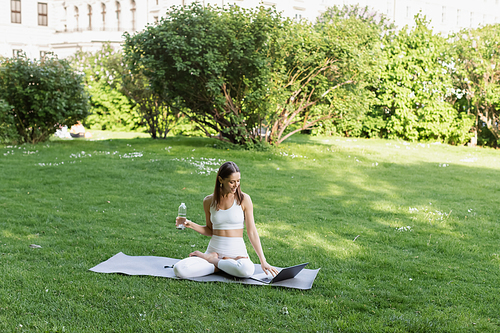 woman in white sportswear sitting in lotus pose near laptop in park