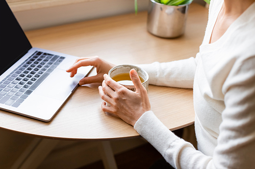 cropped view of woman with clay cup sitting near blurred laptop at home