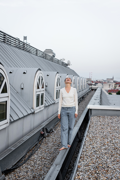 full length of amazed woman looking up while walking barefoot on rooftop