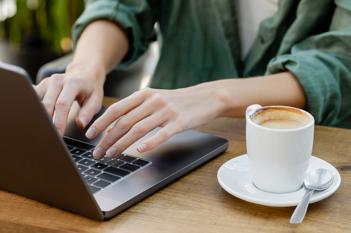 cropped view of woman using laptop near cup of coffee in cafe terrace