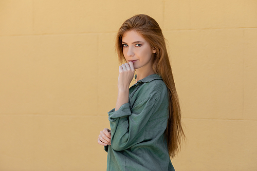 young redhead woman in green linen shirt posing near beige wall