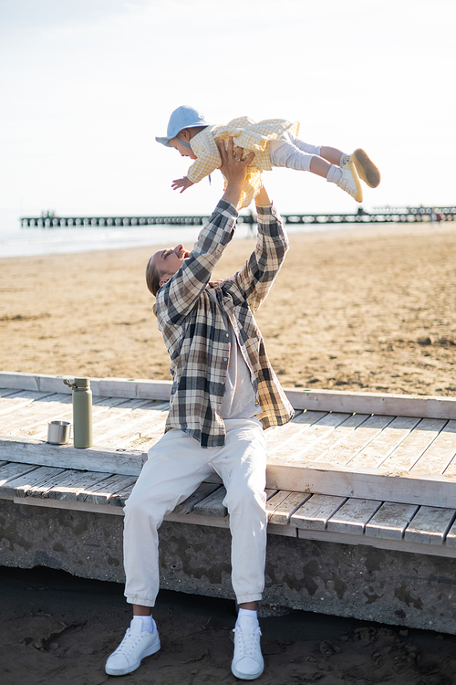 Excited father holding toddler daughter on pier on beach in Treviso