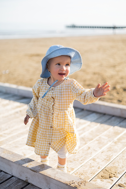 Positive baby girl in panama hat looking away on pier in Treviso
