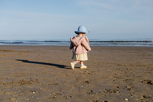 Baby girl in panama hat walking on beach in Italy