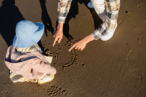 High angle view of man drawing heart sign on sand near toddler daughter