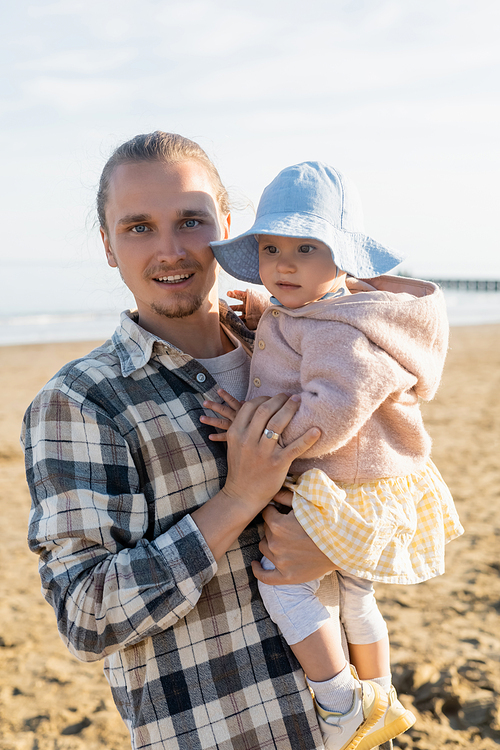 Young father holding baby and looking at camera on beach in Italy