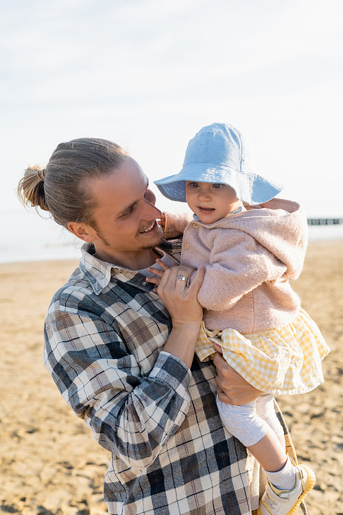 Young long haired dad holding toddler child on beach in Treviso
