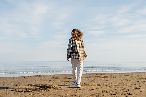Back view of long haired man walking on beach near adriatic sea in Italy