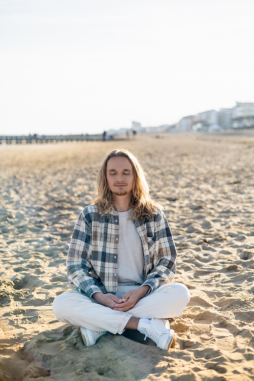 Young man with closed eyes meditating on beach in Italy