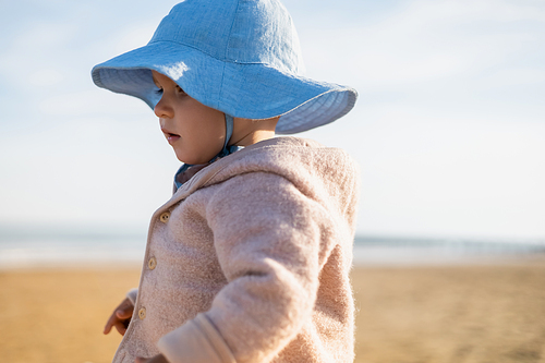 Baby girl in panama hat standing on blurred beach