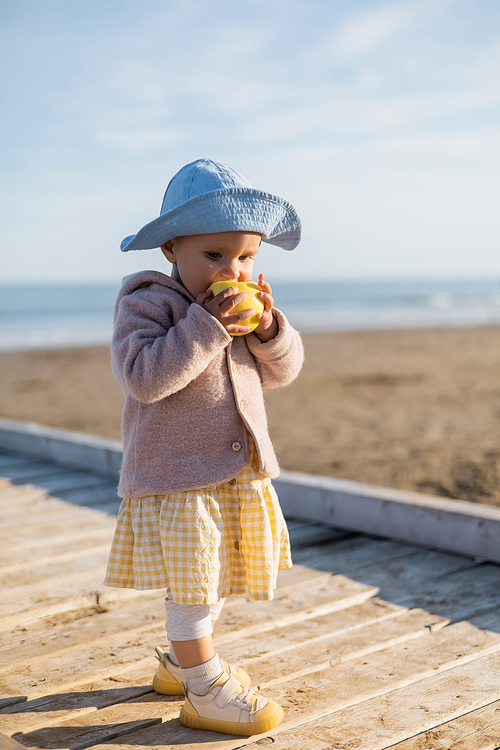 Baby in panama hat eating apple on wooden pier in Treviso