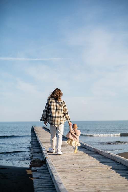 Back view of father and baby girl walking on pier near adriatic sea in Italy