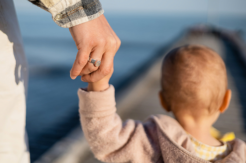 Back view of father holding hand of blurred toddler daughter on pier