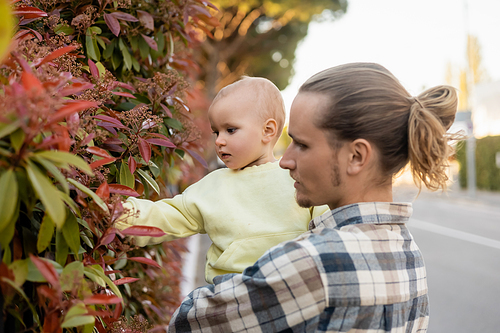 Man holding baby daughter near plant outdoors