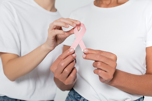 Cropped view of women holding ribbon of breast cancer awareness isolated on grey