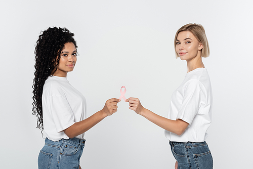 Young interracial women holding pink ribbon of breast cancer awareness isolated on grey