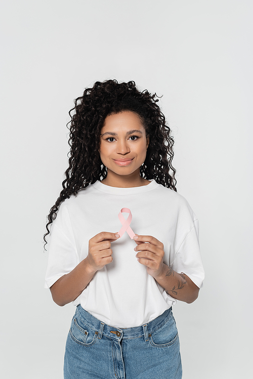 African american woman holding pink ribbon of breast cancer awareness isolated on grey