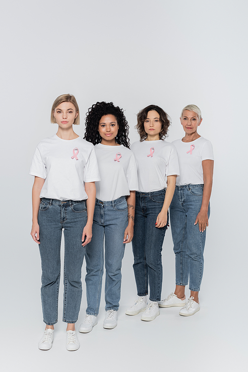 Interracial women with pink ribbons on t-shirts looking at camera on grey background