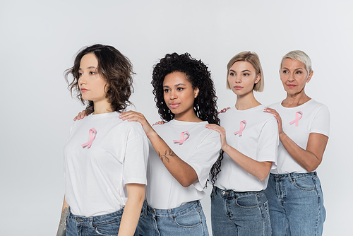 Multiethnic women with ribbons of breast cancer awareness looking away isolated on grey