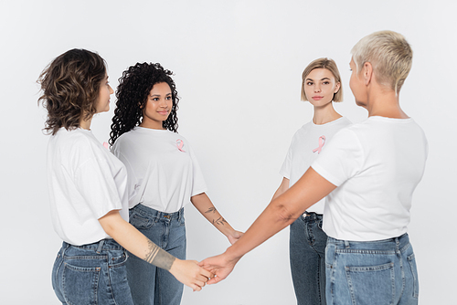 Multiethnic women with pink ribbons on t-shirts holding hands isolated on grey